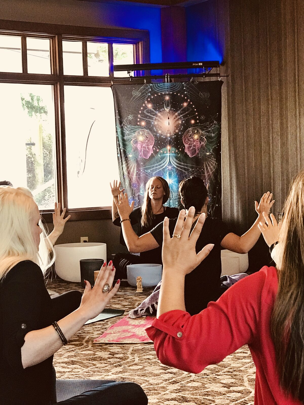A retreat circle with hands raised in front of a tapestry.